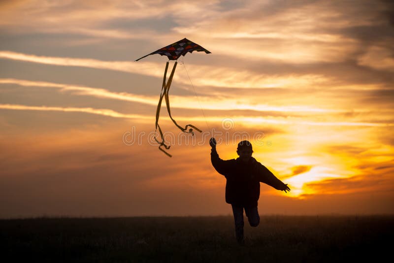 Pilotare un aquilone Il ragazzo funziona attraverso il campo con un aquilone Siluetta di un bambino contro il cielo Tramonto lumi immagine stock libera da diritti Pilotare un aquilone Il ragazzo funziona attraverso il campo con un aquilone Siluetta di un bambino contro il cielo Tramonto lumi immagine stock libera da diritti