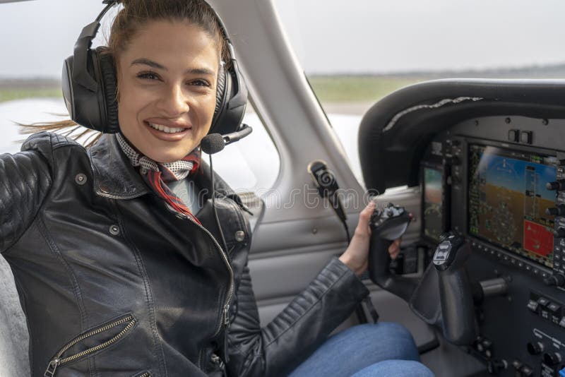 Piloto de sorriso With Headset Sitting da jovem mulher na cabina do piloto do avião fotos de stock Piloto de sorriso With Headset Sitting da jovem mulher na cabina do piloto do avião fotos de stock