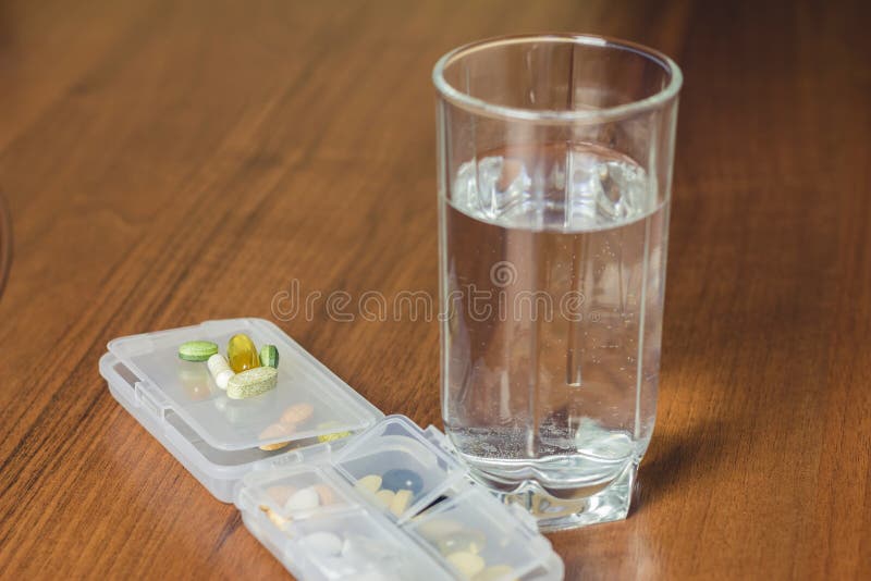Pilules naturelles mélangées de complément alimentaire et de vitamine, verre de l'eau sur la table en bois photo libre de droits Pilules naturelles mélangées de complément alimentaire et de vitamine, verre de l'eau sur la table en bois photo libre de droits