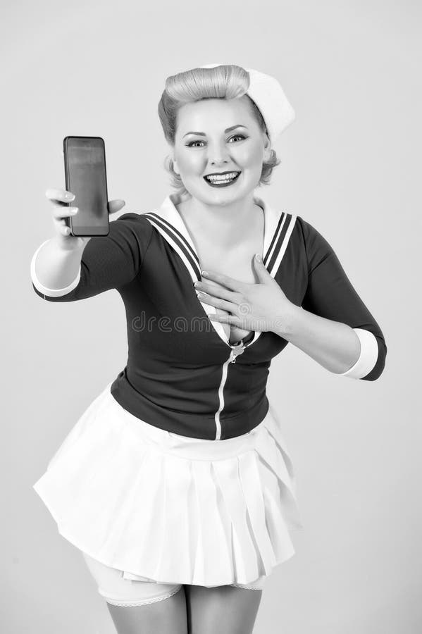 Pin-up styled girl with modern devices. Happy sea woman shows smart-phone and holds hand on chest. Grateful blonde girl with telephone and big smile. Cheerful Woman in anime style isolated on grey isolated in studio with hand on chest. Pin-up styled girl with modern devices. Happy sea woman shows smart-phone and holds hand on chest. Grateful blonde girl with telephone and big smile. Cheerful Woman in anime style isolated on grey isolated in studio with hand on chest