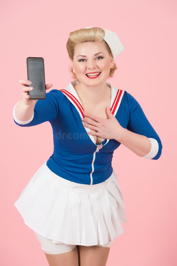 Pin-up styled girl with modern devices. Happy sea woman shows smart-phone and holds hand on chest. Grateful blonde girl with telephone and big smile. Cheerful Woman in anime style isolated on pink. Pin-up styled girl with modern devices. Happy sea woman shows smart-phone and holds hand on chest. Grateful blonde girl with telephone and big smile. Cheerful Woman in anime style isolated on pink.