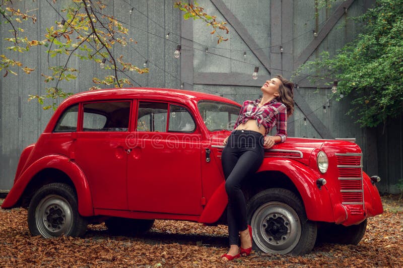 Pin-up-Girl in den Jeans und in einem karierten Hemd lehnt sich auf einem russischen roten Retro- Auto stockfoto Pin-up-Girl in den Jeans und in einem karierten Hemd lehnt sich auf einem russischen roten Retro- Auto stockfoto