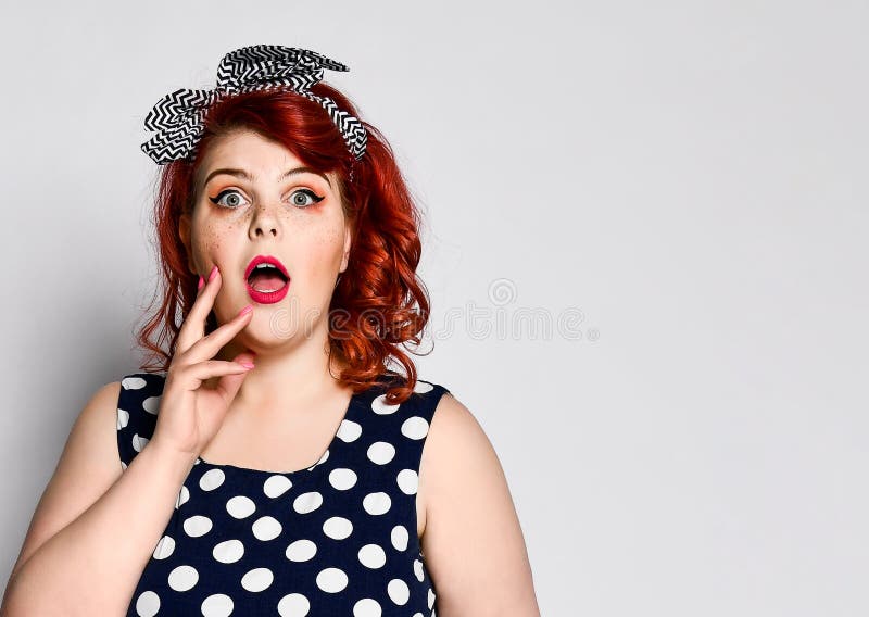 Pin up redhead woman portrait. Beautiful retro female in polka dot dress with red lips and old fashion hairstyle