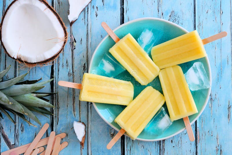 Pineapple coconut popsicles on a plate. Top view scene over a blue wood background. Fruit scene stock images, royalty-free photos and pictures