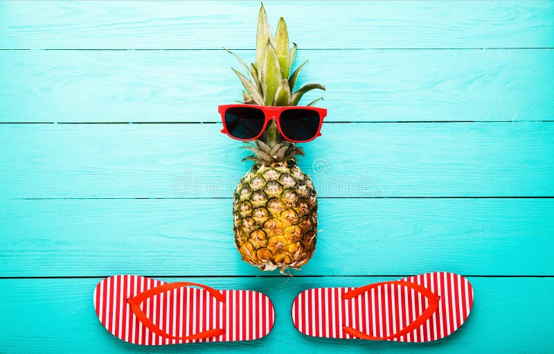 Pineapple with glasses and slippers on blue wooden background. Copy space and top view