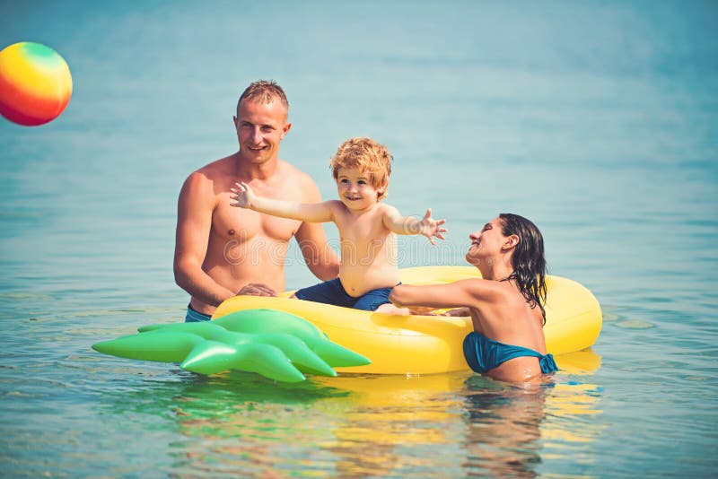 Pineapple inflatable or air mattress. Father and mother with son play ball in water. Maldives or Miami beach activity