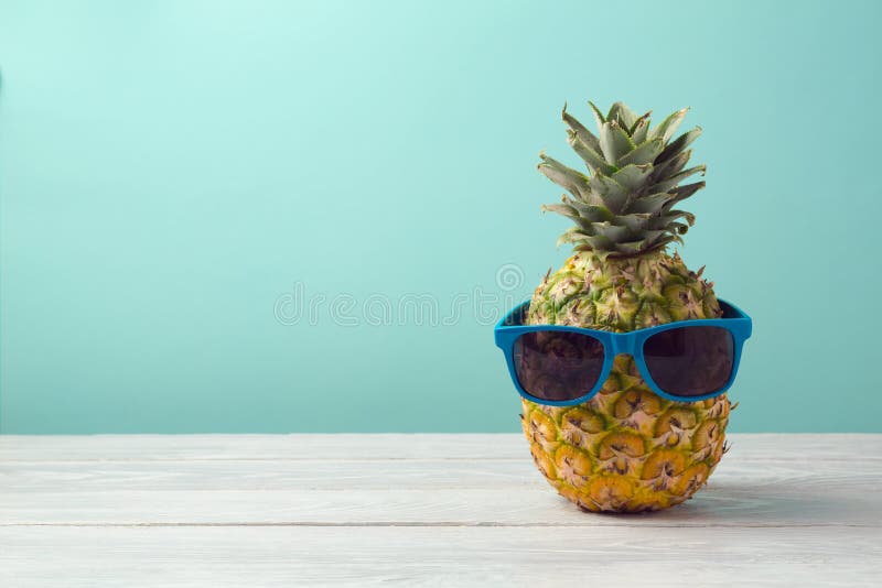 Pineapple with sunglasses on wooden table over mint background. Tropical summer vacation and beach party