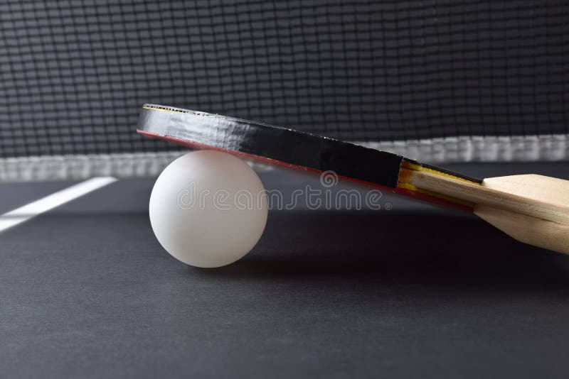 Ping-pong paddle resting on white ball on black game table stock photo
