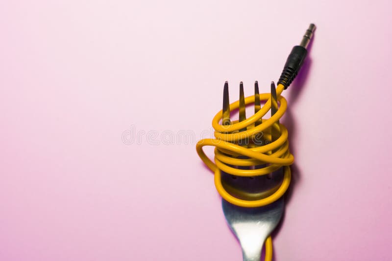 Pink background. Red, pink, yellow headphone cable is wound on silver fork. Spaghetti.