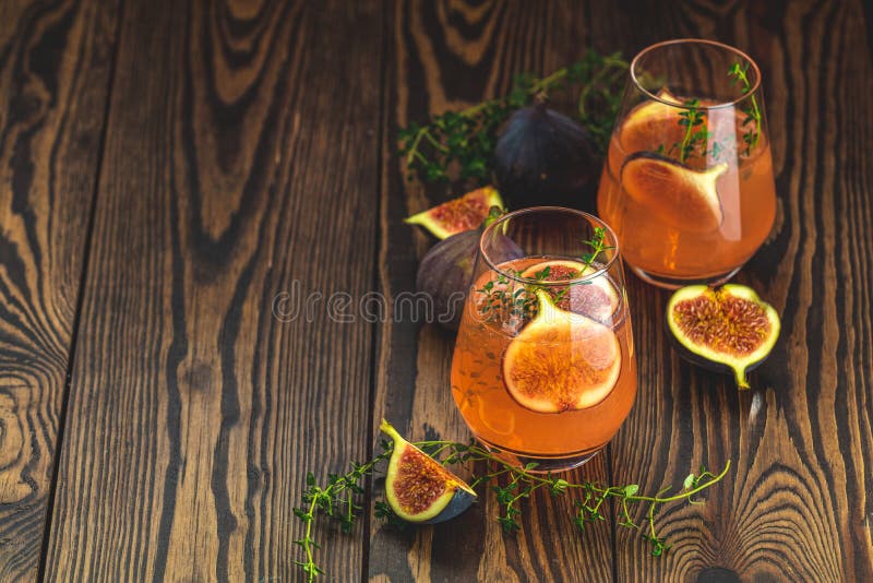 Pink cocktail with fig, thyme and ice in glass on dark wooden background, close up. Summer drinks and alcoholic cocktails.