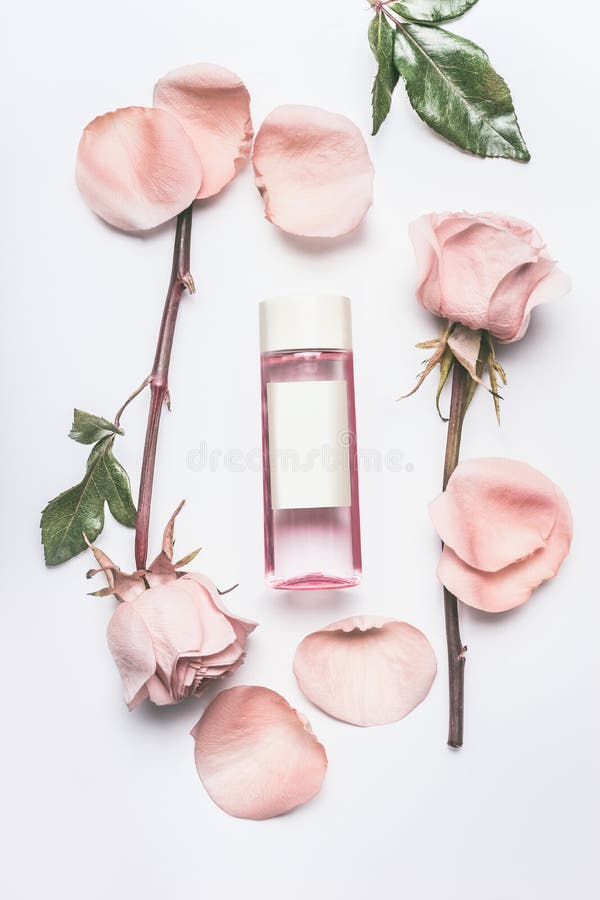 Pink cosmetic bottle with facial roses water or toner with essential oil , flowers and petals on white desk background, top view, branding mock up and copy space. Roses essence