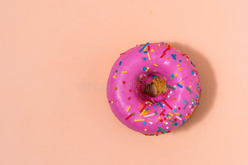 Pink donut with colorful sprinkles on pastel beige background stockfotografie