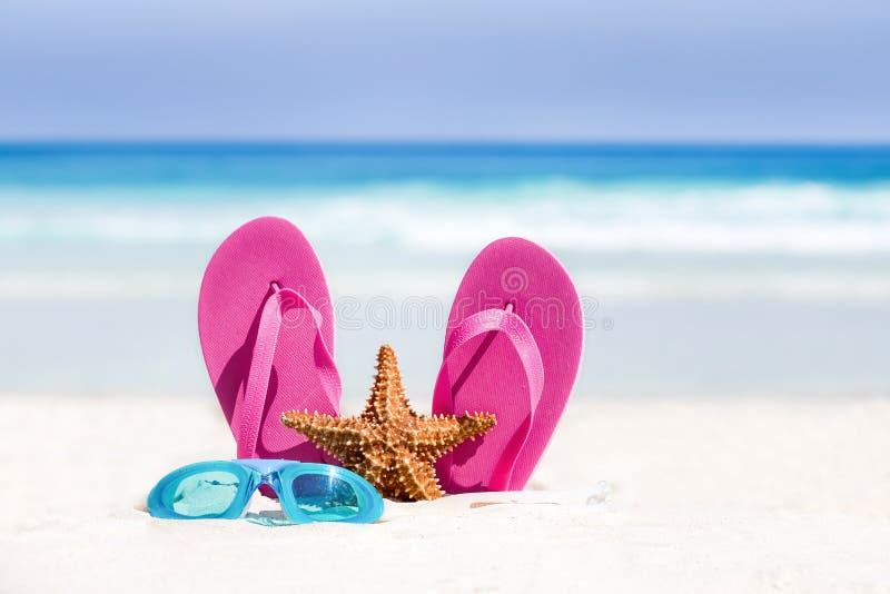 Pink flip flops, swimming glasses and starfish on white sandy beach. Summer vacation concept