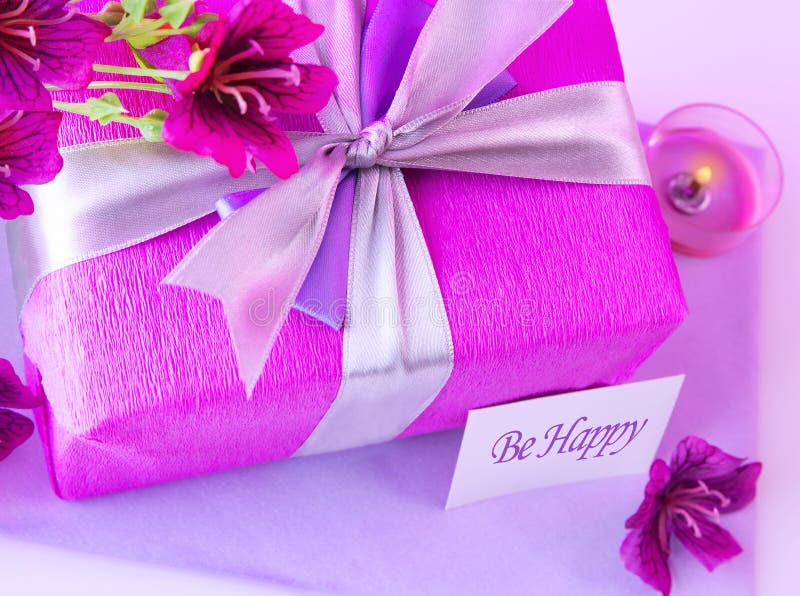 Picture of big pink present box, candle and purple flowers on the table at home, paper greeting card, happy mothers day, romantic holiday, gift for birthday, wedding day, romance and love concept. Picture of big pink present box, candle and purple flowers on the table at home, paper greeting card, happy mothers day, romantic holiday, gift for birthday, wedding day, romance and love concept