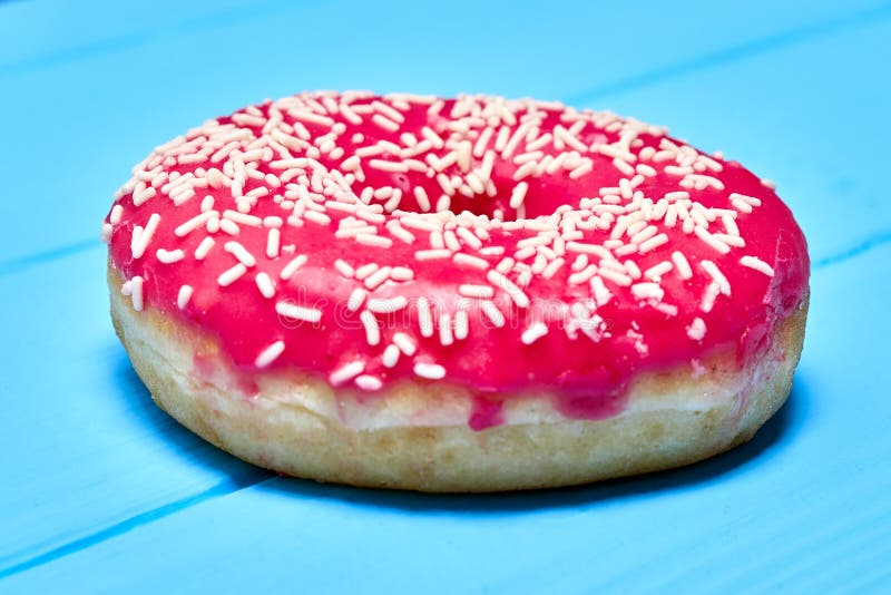 Pink glazed donut onone pink glazed donut on a blue background, sprinkled with coconut a blue background