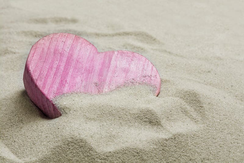 Pink heart made of wood in the sand of a beach, love concept with copy space