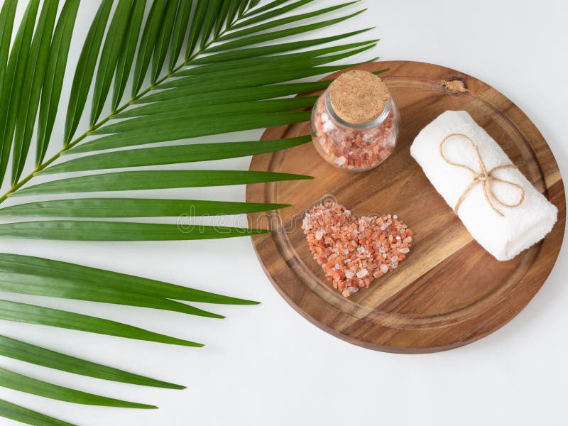 Pink Himalayan salt and towel on wooden plank, monstera and palm leaves