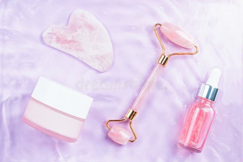 Pink hyaluronic acid serum, rose quartz roller, gua sha and face cream in water, top view. Anti aging cosmetics in pink water, top