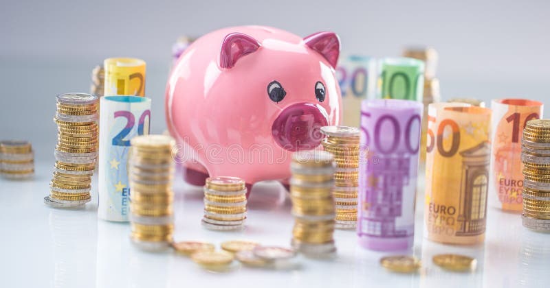 Pink piggy bank in the middle of rolled euro banknotes and towers with coins stock photo Pink piggy bank in the middle of rolled euro banknotes and towers with coins stock photo