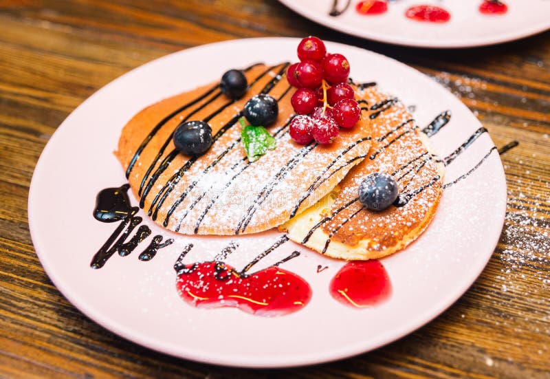 Pink plate with puffed pancakes with berries, sprinkled with powdered sugar, chocolate sauce stock photography Pink plate with puffed pancakes with berries, sprinkled with powdered sugar, chocolate sauce stock photography