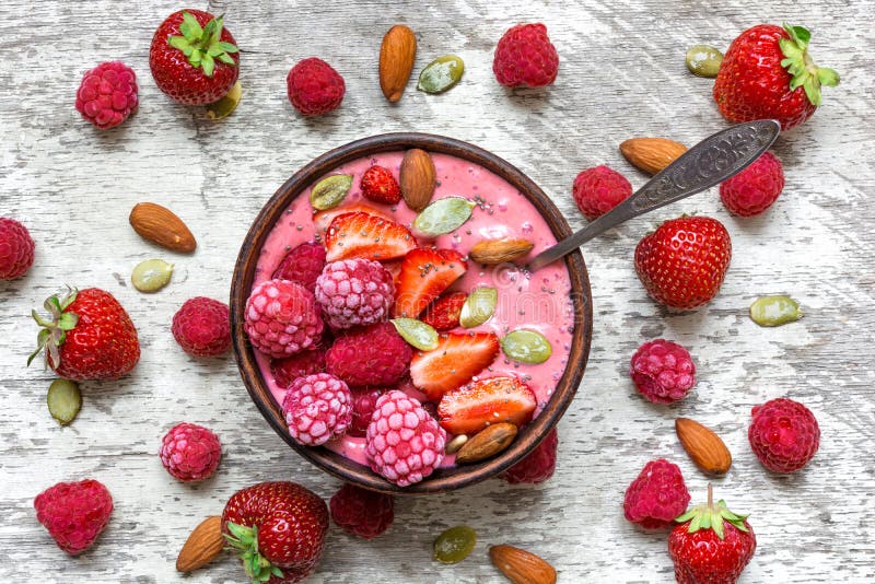 Pink raspberries and strawberry fruit smoothie or milk shake in a bowl with berries, nuts and seeds