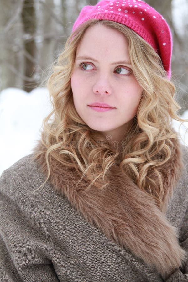 Portrait of a slightly smiling, wholesome, beautiful young woman wearing a fur jacket and pink beret in a snowy forest looking off to the side. Portrait of a slightly smiling, wholesome, beautiful young woman wearing a fur jacket and pink beret in a snowy forest looking off to the side.