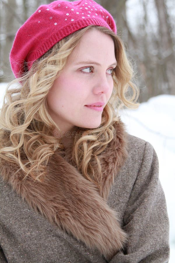 Portrait of a happy, smiling, wholesome, beautiful young woman wearing a fur jacket and pink beret in a snowy forest looking off to the side. Portrait of a happy, smiling, wholesome, beautiful young woman wearing a fur jacket and pink beret in a snowy forest looking off to the side..