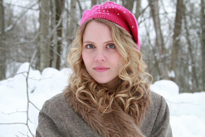 Portrait of a slightly smiling, wholesome, beautiful young woman wearing a fur jacket and pink beret in a snowy forest. Portrait of a slightly smiling, wholesome, beautiful young woman wearing a fur jacket and pink beret in a snowy forest.