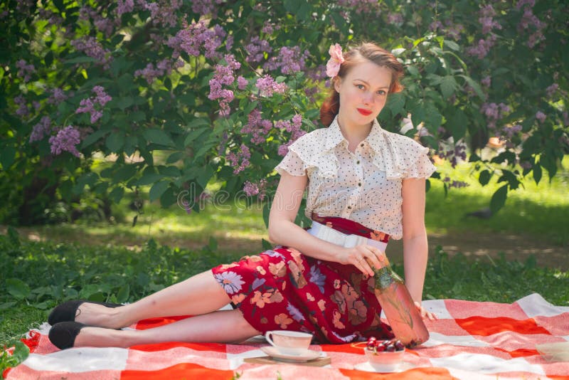 Pretty young pin up girl having rest on the nature. happy slim young woman wearing vintage dress sitting on the tartan plaid and relaxing by summer day alone. alone. Pretty young pin up girl having rest on the nature. happy slim young woman wearing vintage dress sitting on the tartan plaid and relaxing by summer day alone. alone