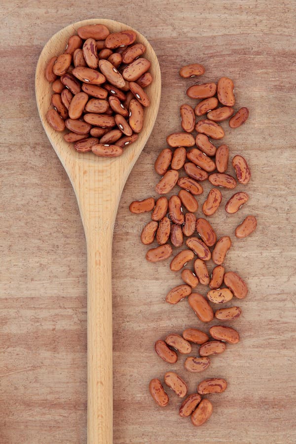Pinto bean pulses in a wooden spoon over papyrus background. Pinto bean pulses in a wooden spoon over papyrus background.