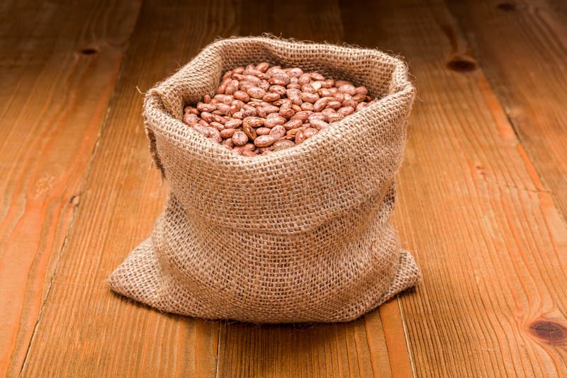 Loose dry pinto beans in burlap sack on wooden board background. Loose dry pinto beans in burlap sack on wooden board background