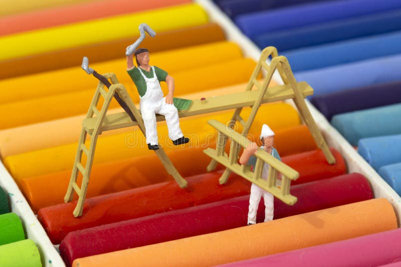 Miniature scale model painters and decorators with ladders on a set of oil pastel crayons.  Decorating concept. Miniature scale model painters and decorators with ladders on a set of oil pastel crayons.  Decorating concept