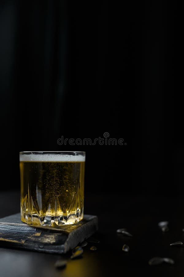 Pionowe ujęcie szklanki piwa alkoholowego lub bezalkoholowego stojącej na czarnym drewnianym stole fotografia royalty free