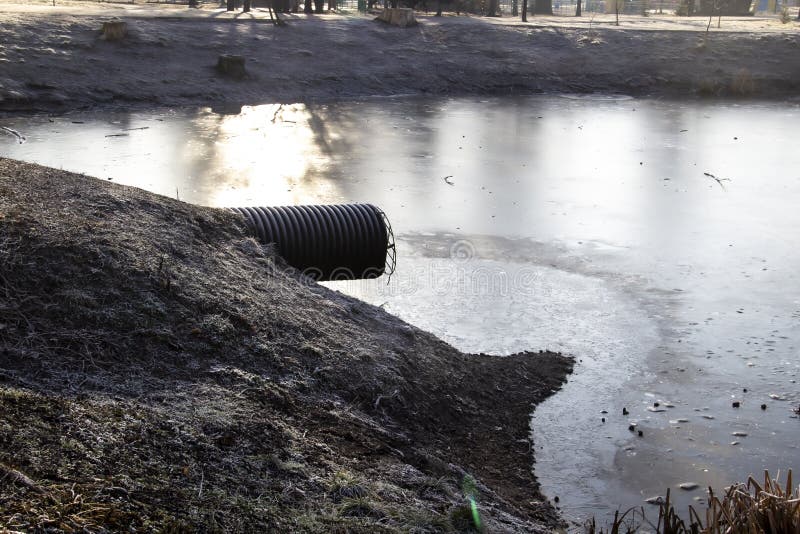 Pipe for draining sewage into a frozen lake in a park. Waste Discharge to the lake royalty free stock photos Pipe for draining sewage into a frozen lake in a park. Waste Discharge to the lake royalty free stock photos