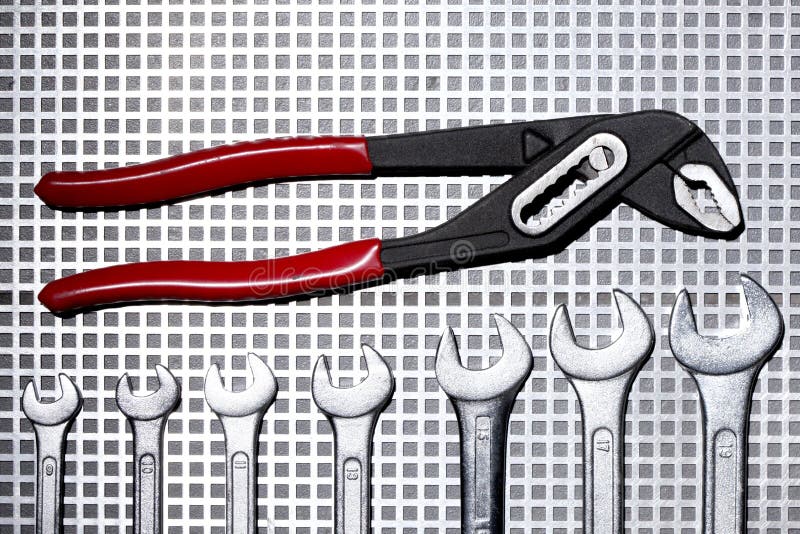 Pipe Wrench and Group of Different Size Wrenches on a Metallic Grid