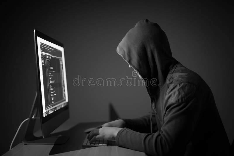 Pirata informatico di computer in cappuccio che funziona nel codice della stanza scura sulle reti dell'incisione e del pc fotografia stock Pirata informatico di computer in cappuccio che funziona nel codice della stanza scura sulle reti dell'incisione e del pc fotografia stock