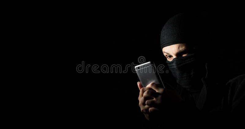 Pirata informático usando el teléfono elegante Muchacha adulta joven en ropa negra con miradas ocultadas de la cara en la pantall imagen de archivo libre de regalías Pirata informático usando el teléfono elegante Muchacha adulta joven en ropa negra con miradas ocultadas de la cara en la pantall imagen de archivo libre de regalías
