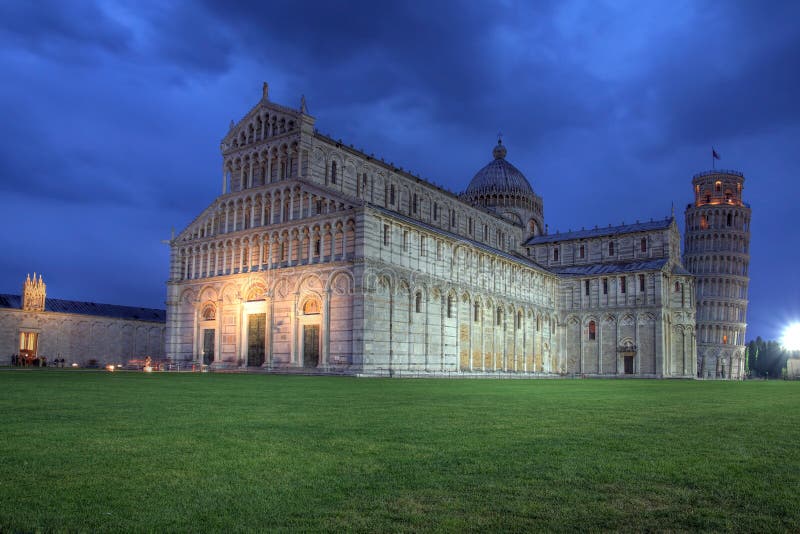 Dramatic sunset on the Square of Miracles (Piazza dei Miracoli) in Pisa, Italy. The Pisa Cathedral (Duomo) dominates the frame, with the famous Leaning Tower (Campanile - free standing bell tower) in the background and the entrance to the Monumental Cemetery (Campo Santo) on the left side. HDR image. Dramatic sunset on the Square of Miracles (Piazza dei Miracoli) in Pisa, Italy. The Pisa Cathedral (Duomo) dominates the frame, with the famous Leaning Tower (Campanile - free standing bell tower) in the background and the entrance to the Monumental Cemetery (Campo Santo) on the left side. HDR image.