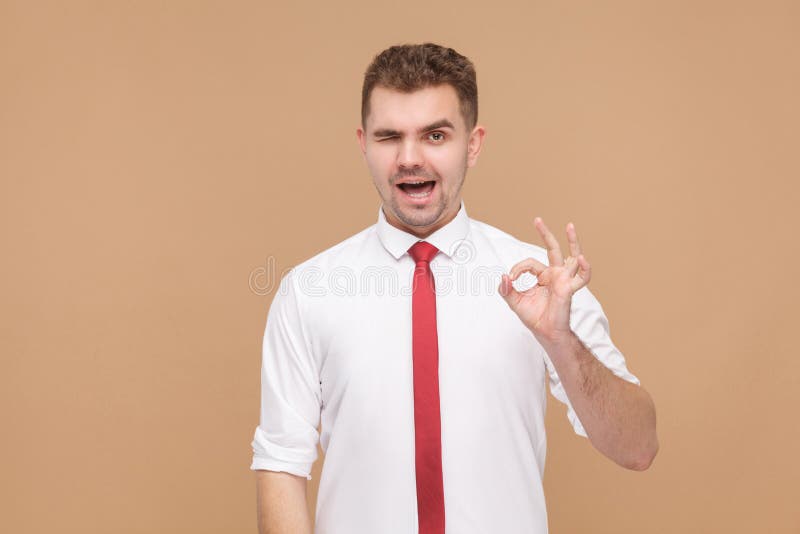 Piscadela atrativa do homem de negócios, sorrindo e mostrando o sinal aprovado imagens de stock Piscadela atrativa do homem de negócios, sorrindo e mostrando o sinal aprovado imagens de stock