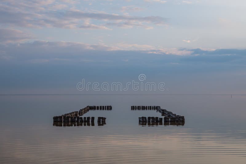 Piscina de madera vieja delante de las nubes de la puesta del sol reflejadas en el agua lisa del lago imagen de archivo Piscina de madera vieja delante de las nubes de la puesta del sol reflejadas en el agua lisa del lago imagen de archivo