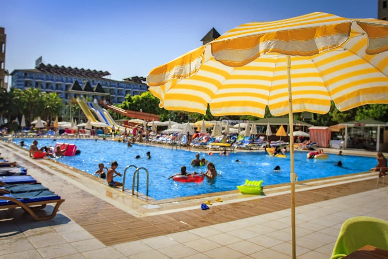 Piscina na estância tropical Guarda-chuva amarelo no fundo borrado de banhar turistas na associação no dia ensolarado brilhante fotografia de stock Piscina na estância tropical Guarda-chuva amarelo no fundo borrado de banhar turistas na associação no dia ensolarado brilhante fotografia de stock