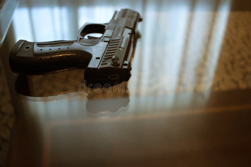 Automatic pistol gun on glass table in bedroom in luxury hotel in silhouette with reflection of window light. Automatic pistol gun on glass table in bedroom in luxury hotel in silhouette with reflection of window light.