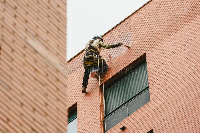 Painter perched hanging on the walls of a building with ropes. Painter perched hanging on the walls of a building with ropes.