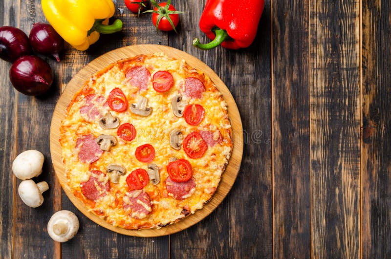 Pizza casalinga con i pomodori ed i funghi su una tavola di legno con le verdure fotografia stock libera da diritti Pizza casalinga con i pomodori ed i funghi su una tavola di legno con le verdure fotografia stock libera da diritti
