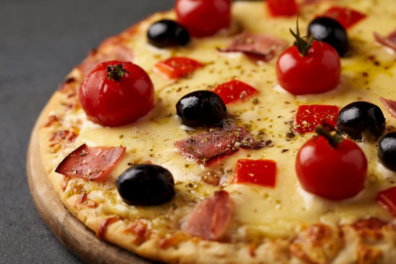 Pizza con el jamón, el queso de la mozzarella, los tomates de cereza, la pimienta roja, las aceitunas negras y el orégano El hoga foto de archivo libre de regalías Pizza con el jamón, el queso de la mozzarella, los tomates de cereza, la pimienta roja, las aceitunas negras y el orégano El hoga foto de archivo libre de regalías
