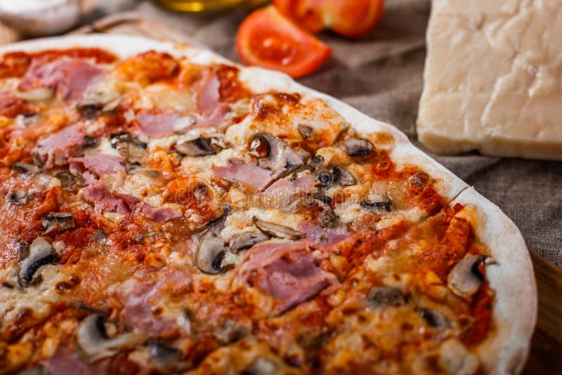 Pizza con il prosciutto, il formaggio, i funghi e la salsa al pomodoro sulla tavola rustica di legno fotografia stock libera da diritti Pizza con il prosciutto, il formaggio, i funghi e la salsa al pomodoro sulla tavola rustica di legno fotografia stock libera da diritti