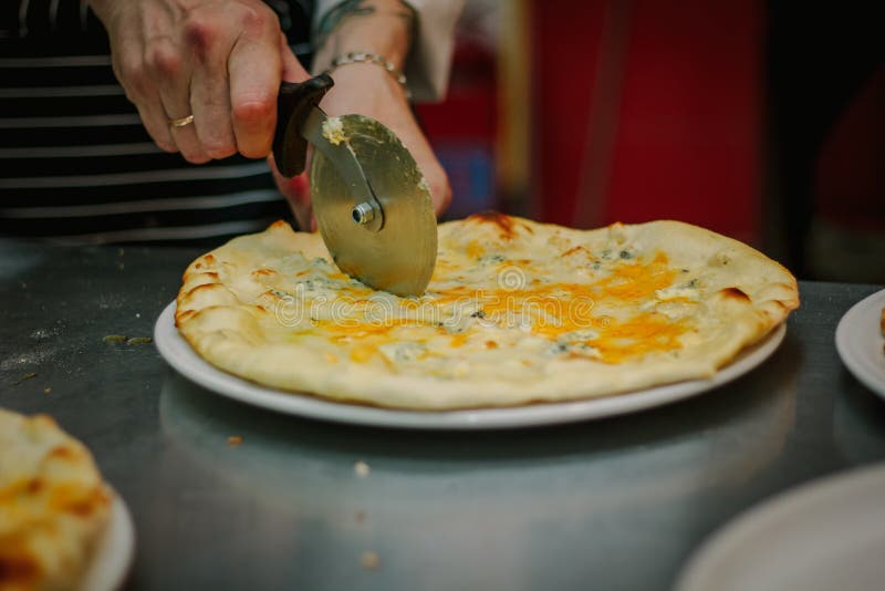 Pizza de coupe de chef avec le coupeur ou le couteau rond de pizza photographie stock libre de droits Pizza de coupe de chef avec le coupeur ou le couteau rond de pizza photographie stock libre de droits