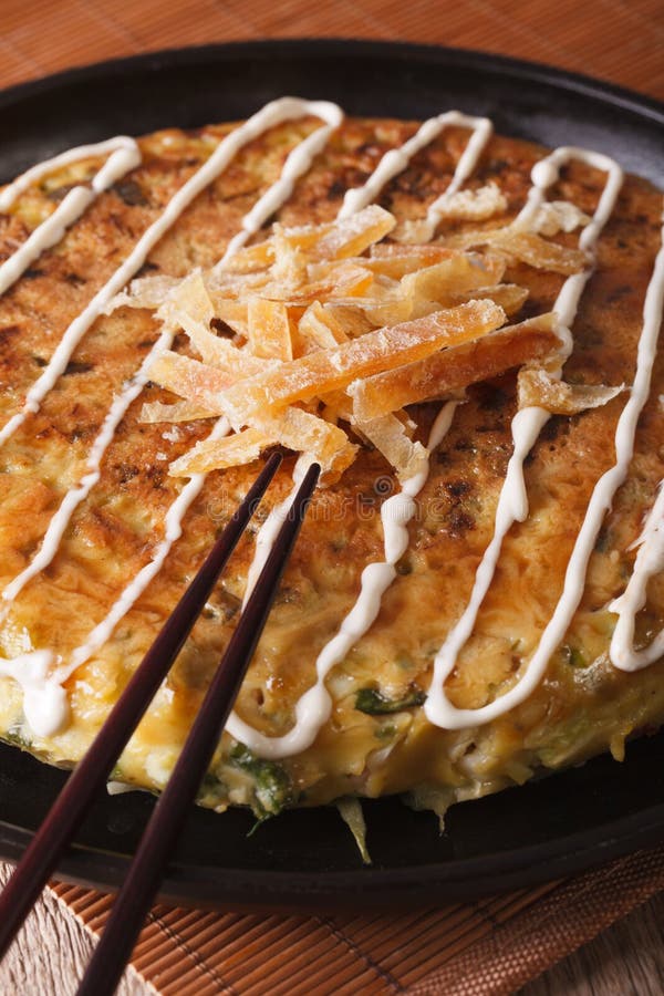 Pizza giapponese: okonomiyaki su un piatto e sui bastoncini verticale fotografia stock libera da diritti Pizza giapponese: okonomiyaki su un piatto e sui bastoncini verticale fotografia stock libera da diritti