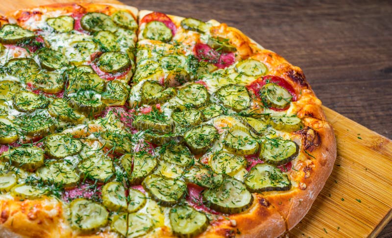 Pizza with Mozzarella cheese, salami, bacon, Tomato sauce, fresh dill, Spices and pickled cucumbers. big dill pizza on wooden tabl