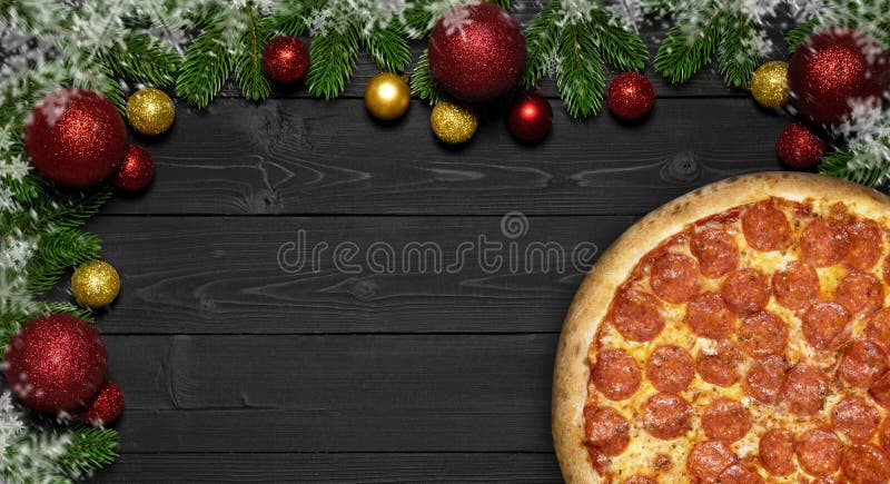 Pizza pepperoni Christmas snowflake with fir branches and new year toy ball, on black wood board table